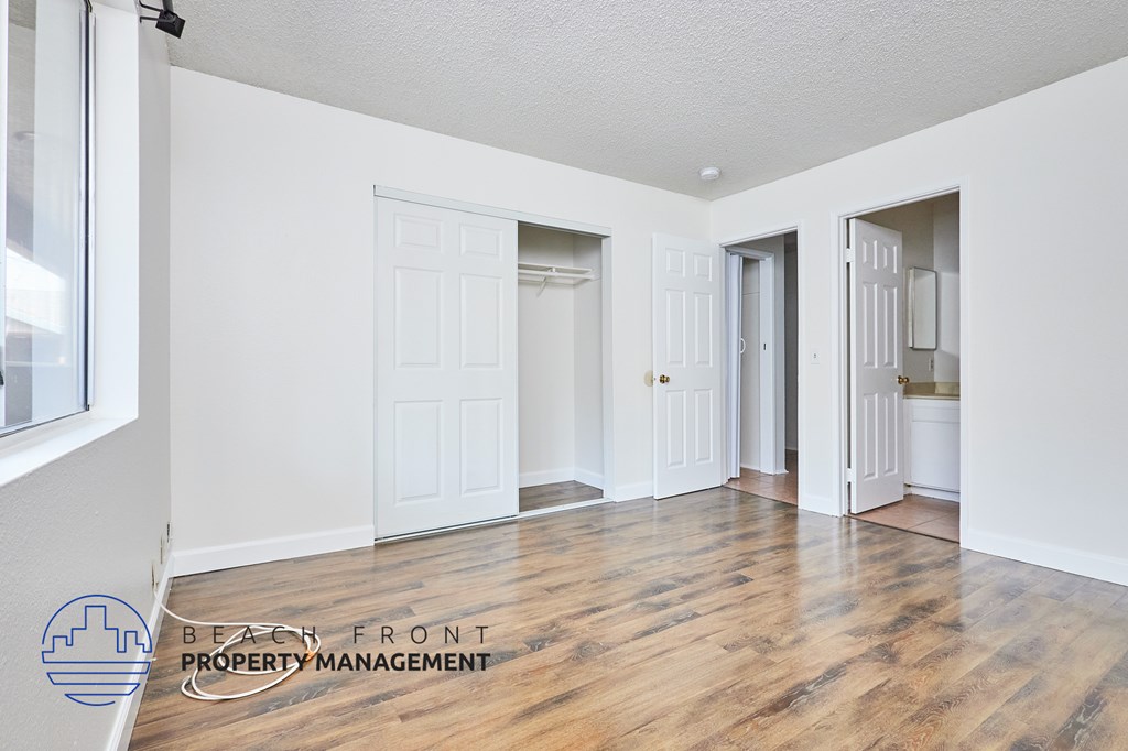 A room with wooden floors and white walls, with a logo for Beach Front Property Management in the bottom left corner.