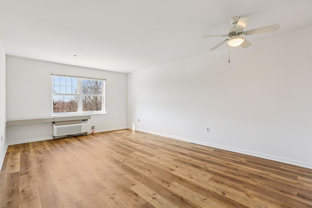 A room with a ceiling fan and a window with a view of trees and a building outside.