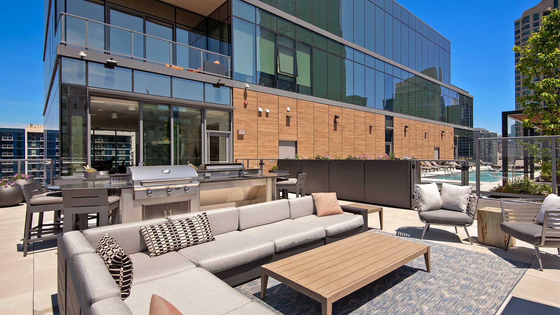 Looking over an outdoor sectional couch at a grilling station behind it. The top of the Hubbard221 tower is behind and the pool deck is off to the right.