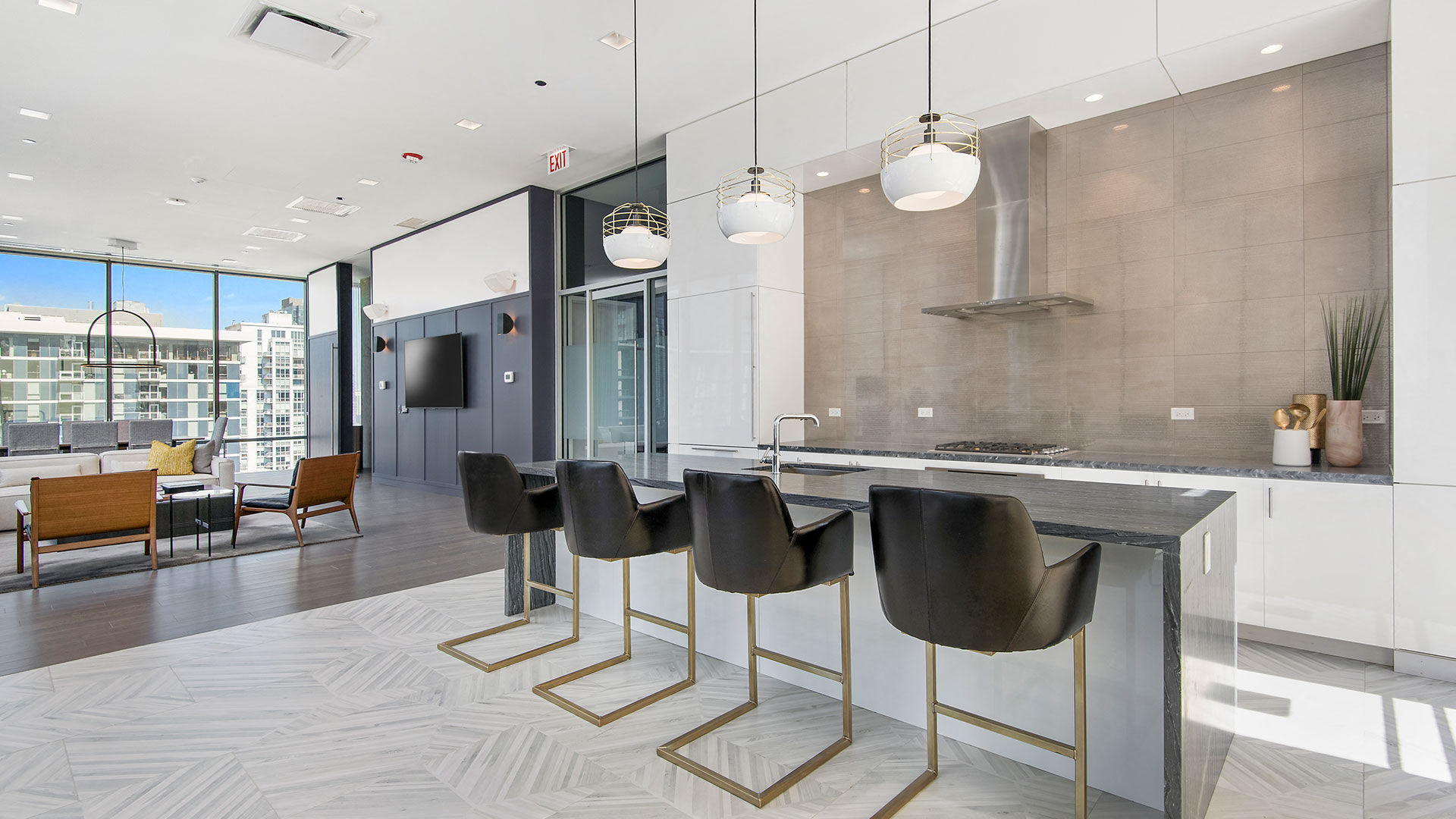Looking across the chef's kitchen island in the kitchen area of the party room. There are four large stools in front of the island. Off to the left is a sitting and dining area.
