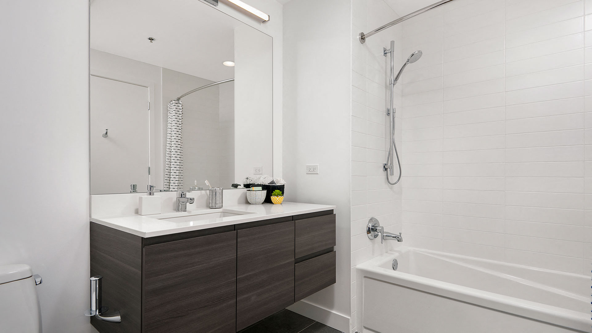 A bathroom in a residence at Hubbard221. The tub and shower is on the right. A floating vanity with single sink and a wall mounted mirror is on the left.