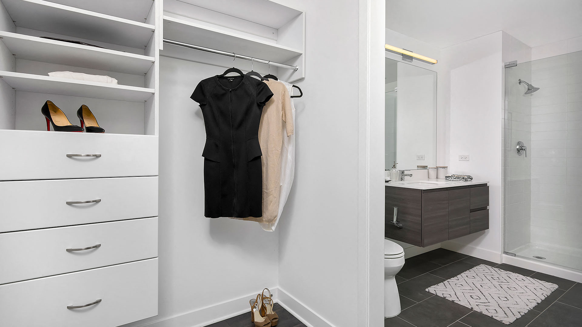 A custom built-in closet is on the left with drawers and a closet rod. On the right, around a small wall is a bathroom with floating vanity and stand-up shower.