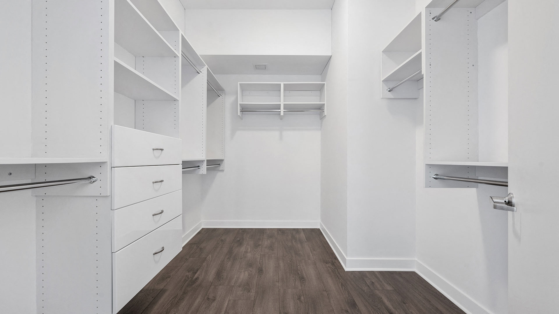Looking into a custom closet in a Hubbard221 residence. There are a variety of shelves, drawers and closet road along all three walls.