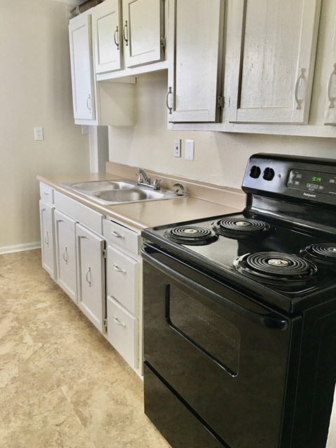 A black stove top oven in a kitchen with white cabinets.