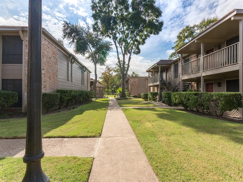 a walkway between two apartment buildings with grass and trees