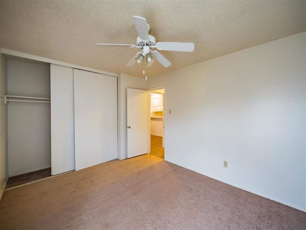 an empty living room with a ceiling fan and a closet