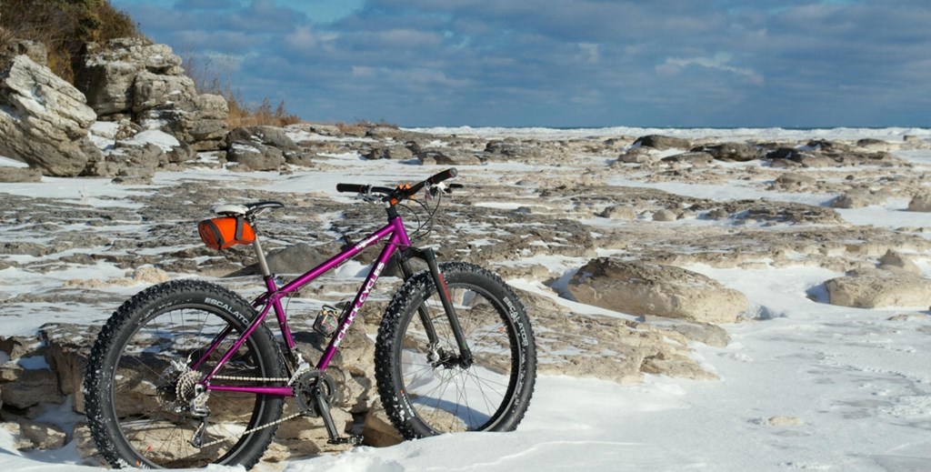 a pink bike parked in the snow on a rocky beach