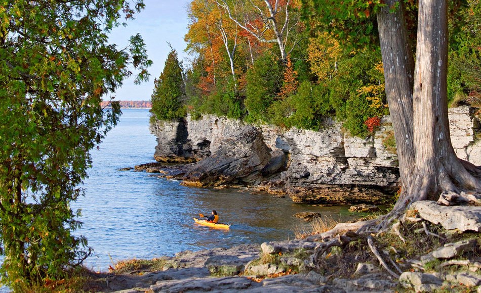 a person in a kayak in the water next to a rocky shore with trees