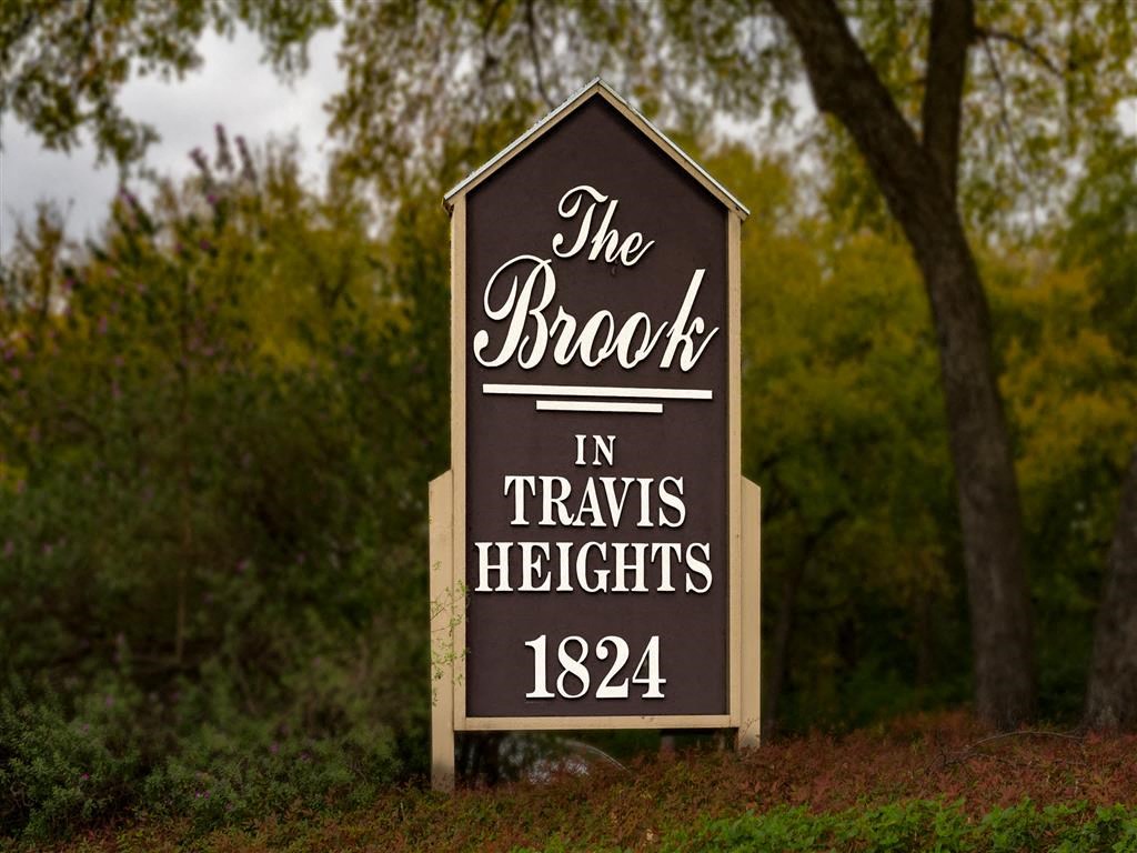 a sign for the brook in travis heights in front of some trees
