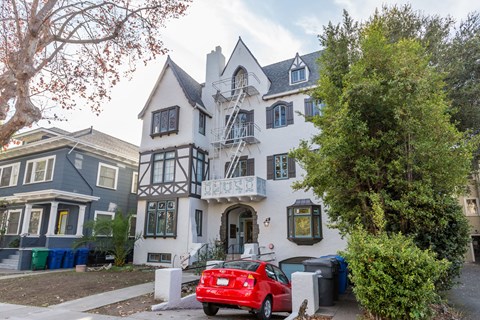 A red car is parked in front of a white and black house.