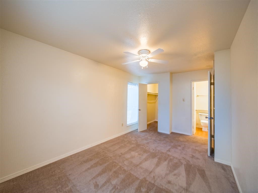 an empty living room with a ceiling fan and a door to a bathroom