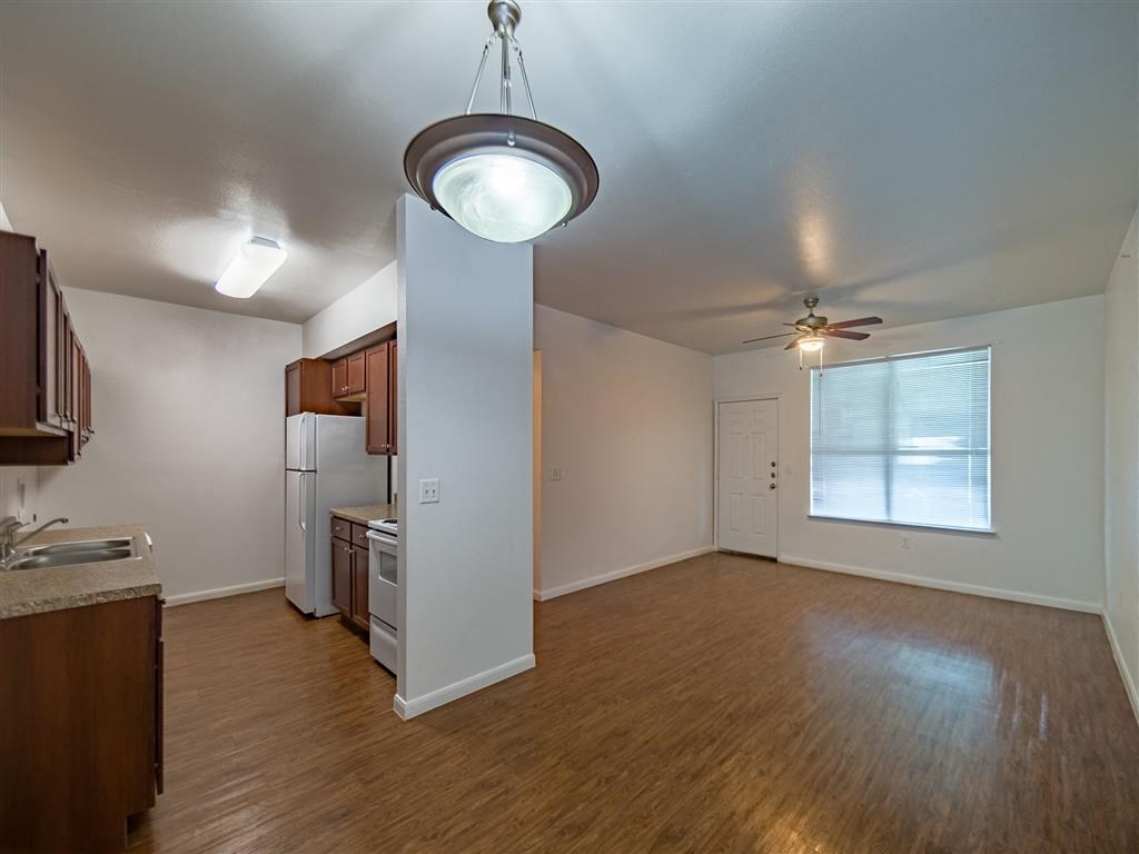 an empty living room with a kitchen and a ceiling fan
