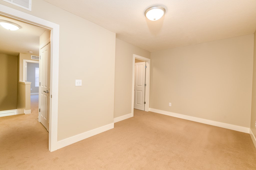 an empty living room with a door to a hallway and a door into a bedroom