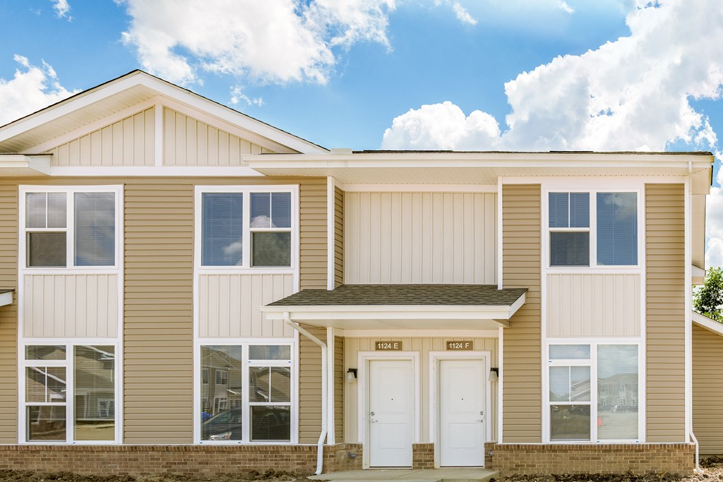 the front of a tan house with two white doors