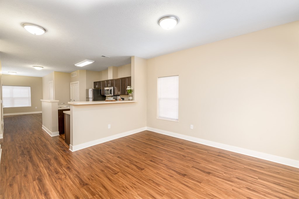 an empty living room with wood flooring and a kitchen