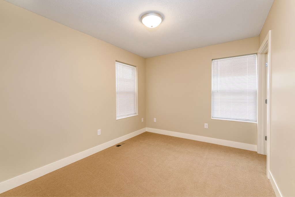 an empty room with beige carpet and two windows