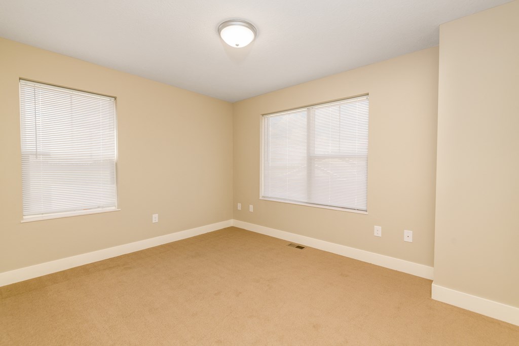 an empty room with two windows and a carpet