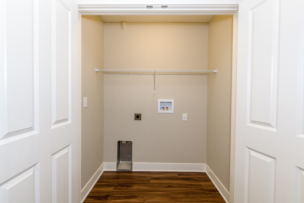 a hallway with a white wall and wood floor and a trash can in the corner
