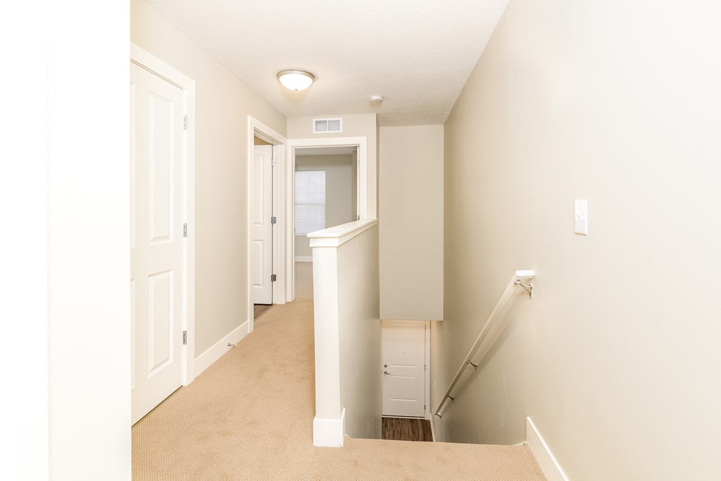 an empty hallway with a staircase and a door to a closet