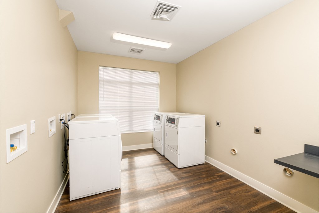 an empty laundry room with two washers and dryers and a window