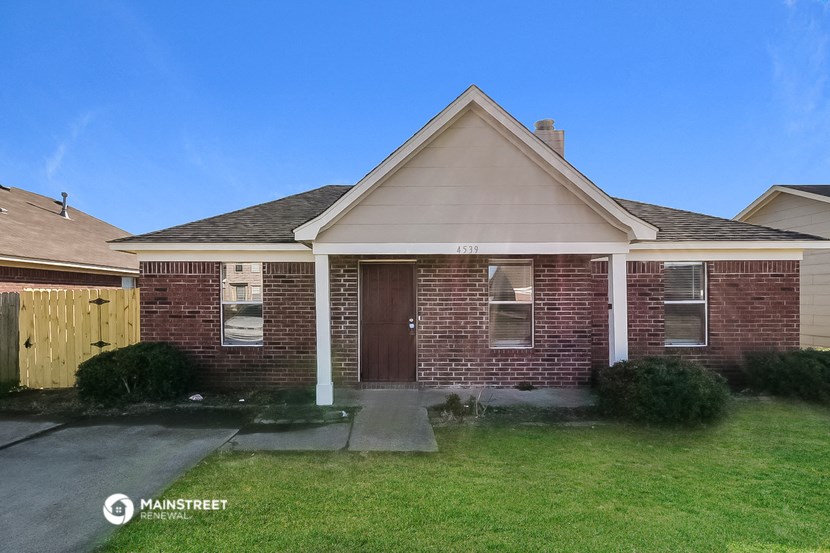 the front of a brick house with a yard and a wooden fence
