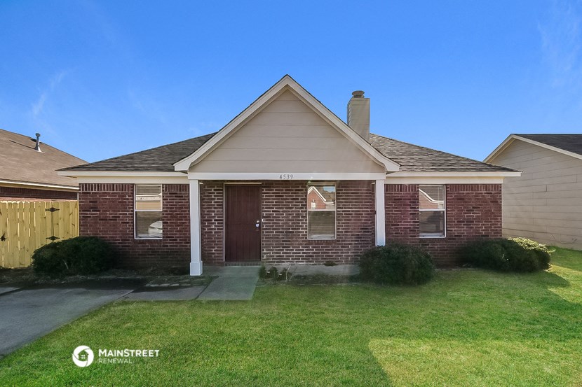 the front of a brick house with a lawn and a wooden fence