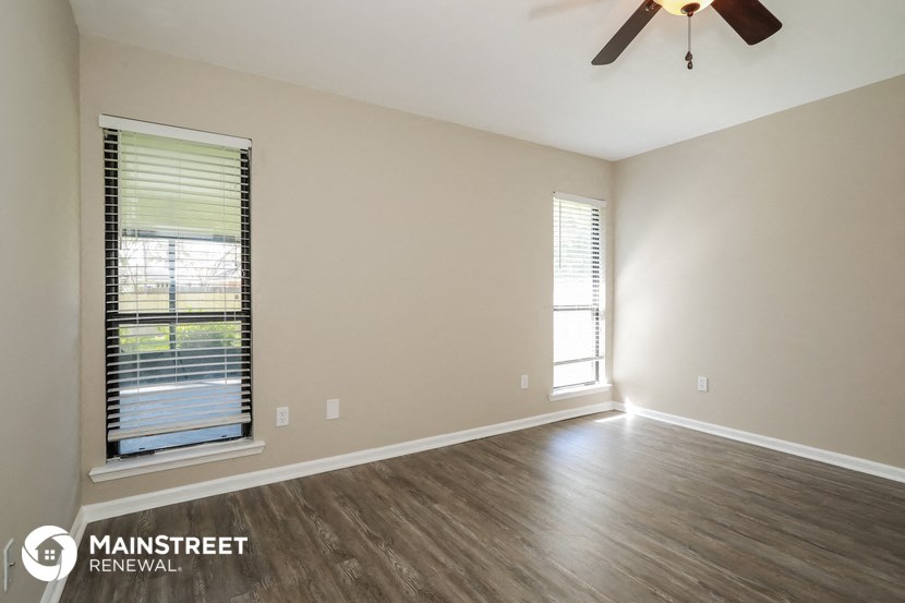 the spacious living room with wood flooring and a ceiling fan