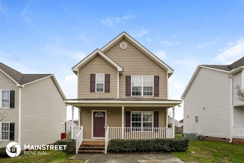 a tan house with a porch and a white fence