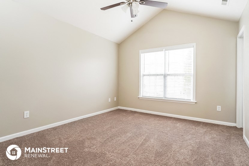 the spacious living room with carpeted floors and a ceiling fan