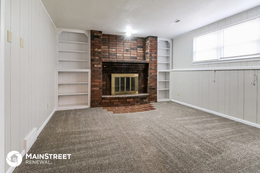 a living room with a brick fireplace and white walls and carpet