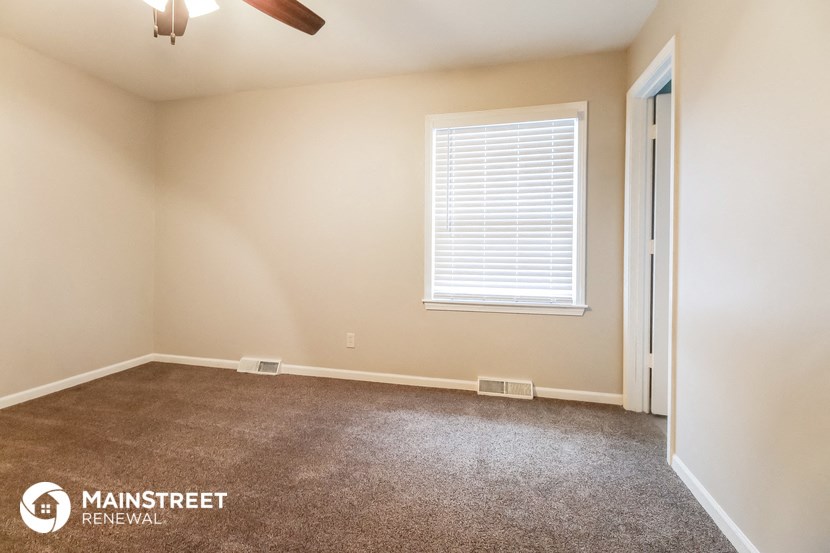 the spacious living room with carpeted flooring and a window