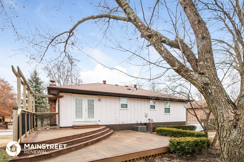 a small white house with a deck and a tree