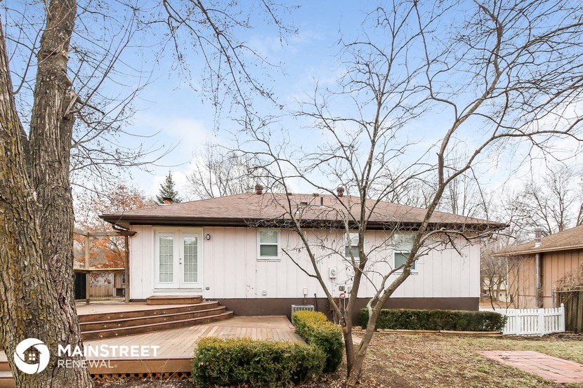 a small white house with a deck and trees