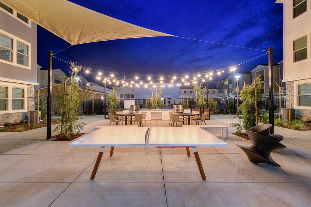 Ping pong table at night with a view of the white lights strung back and forth across the BBQ area at Morgan Ranch Apartments, California