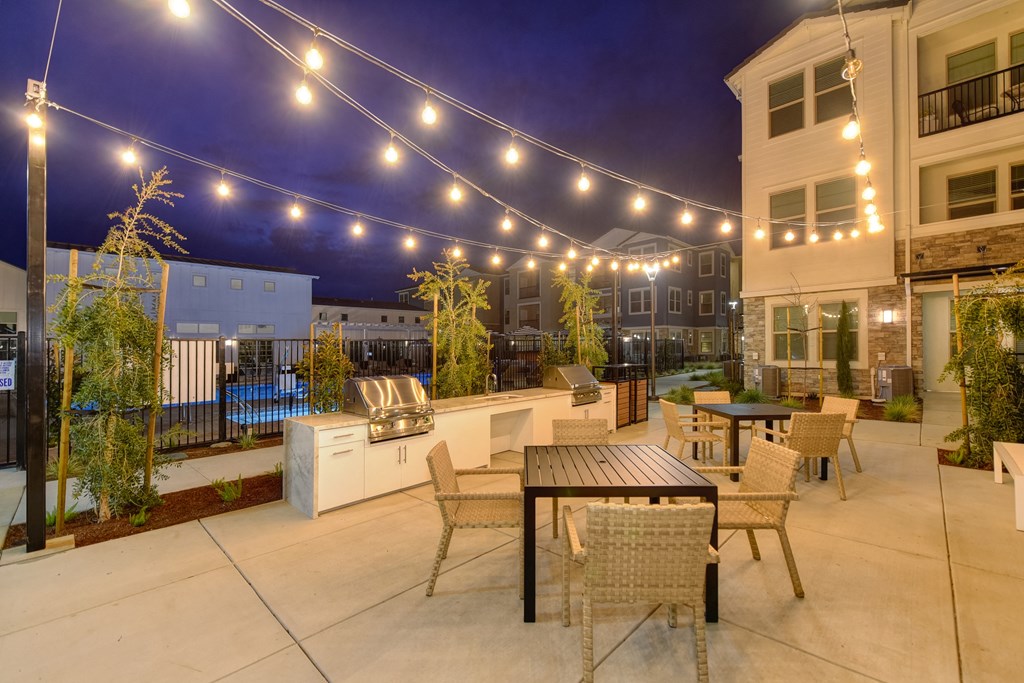 Two Gas BBQ's  and outdoor seating area at nighttime. White lights are strung back and forth across that light up the area at Morgan Ranch Apartments, California, 95037