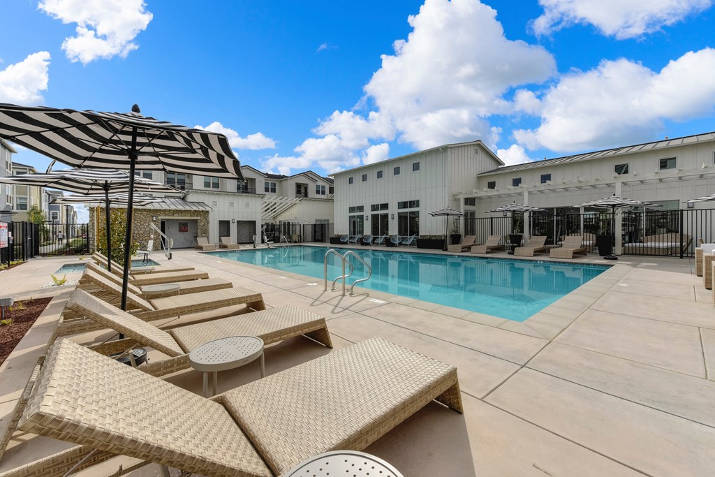Outdoor pool area with tan colored lounge seating and black & white pool-side umbrellas at Morgan Ranch Apartments, Morgan Hill, California