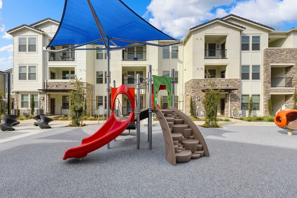 Outdoor playground, Red Slide,  and blue UV sun trap over it at Morgan Ranch Apartments, California