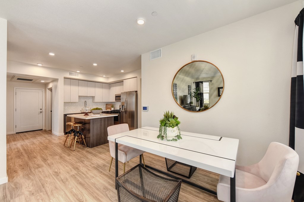 Dining area with table and chairs.  Round wall mirror on dining room wall and kitchen island in the background at Morgan Ranch Apartments, Morgan Hill, California