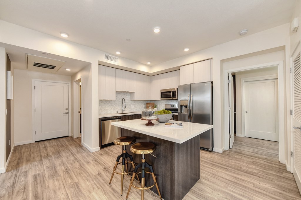 Kitchen with hardwood inspired floors and large island counter with two stools at Morgan Ranch Apartments, California