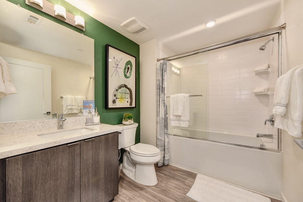 Bathroom with green accent wall.  White tub/shower combination with sliding shower doors and hardwood inspired flooring at Morgan Ranch Apartments, Morgan Hill, California