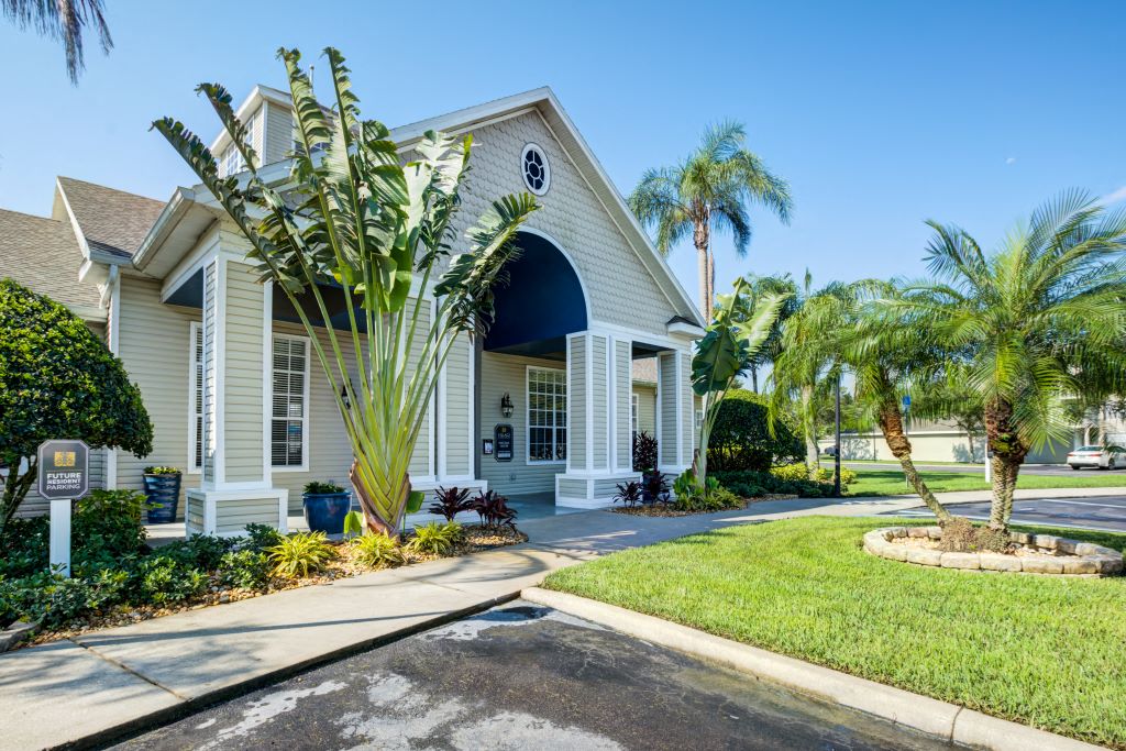 Apartments in Lakeland, FL for Rent - Village at Lake Highland - Clubhouse Exterior with Pale Walls, Path, Greenery, and Surrounding Palm Trees
