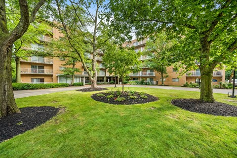 a yard with trees in front of an apartment building