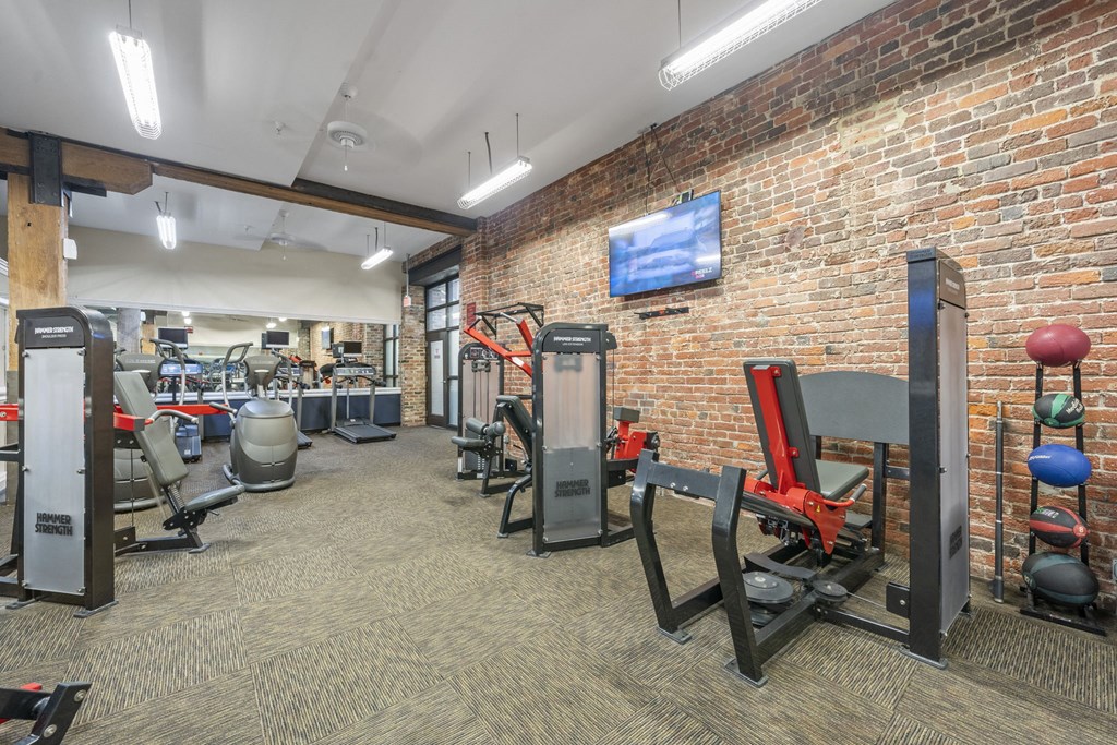 a gym with cardio equipment and a brick wall with a tv