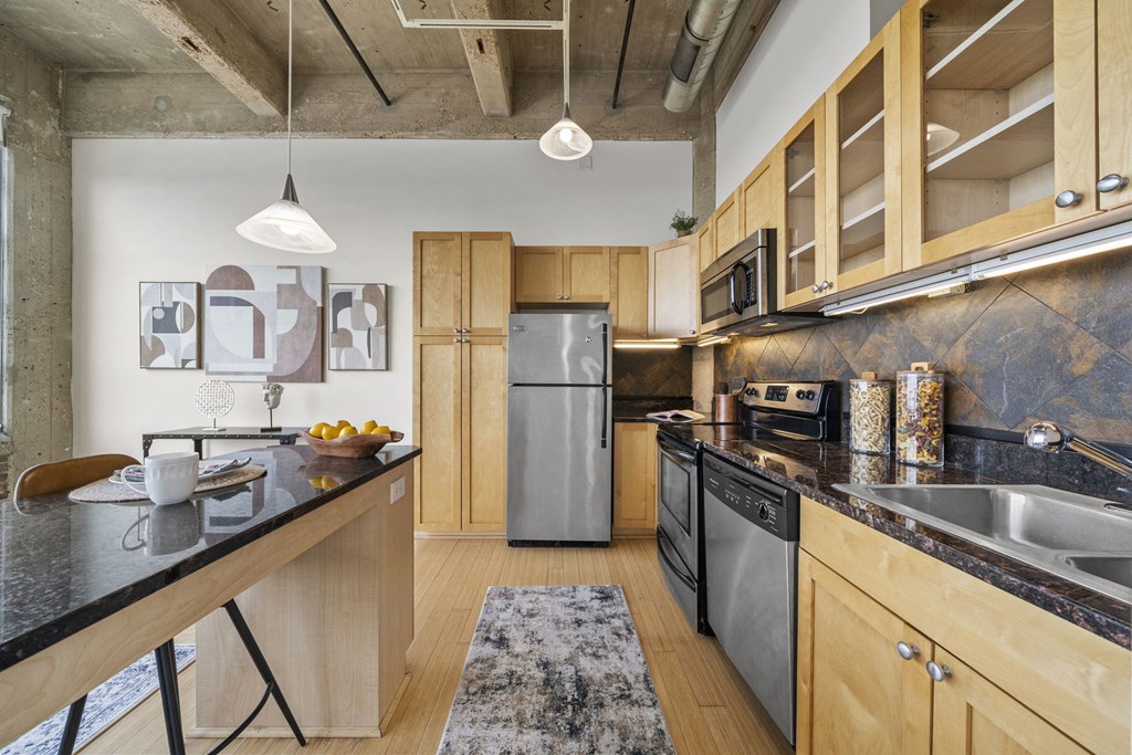 a kitchen with wooden cabinets and black counter tops and a stainless steel refrigerator