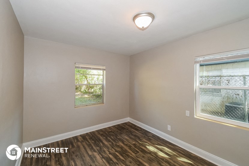 the interior of an empty room with wood flooring and two windows
