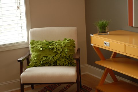 a chair with a green pillow in a room with a desk