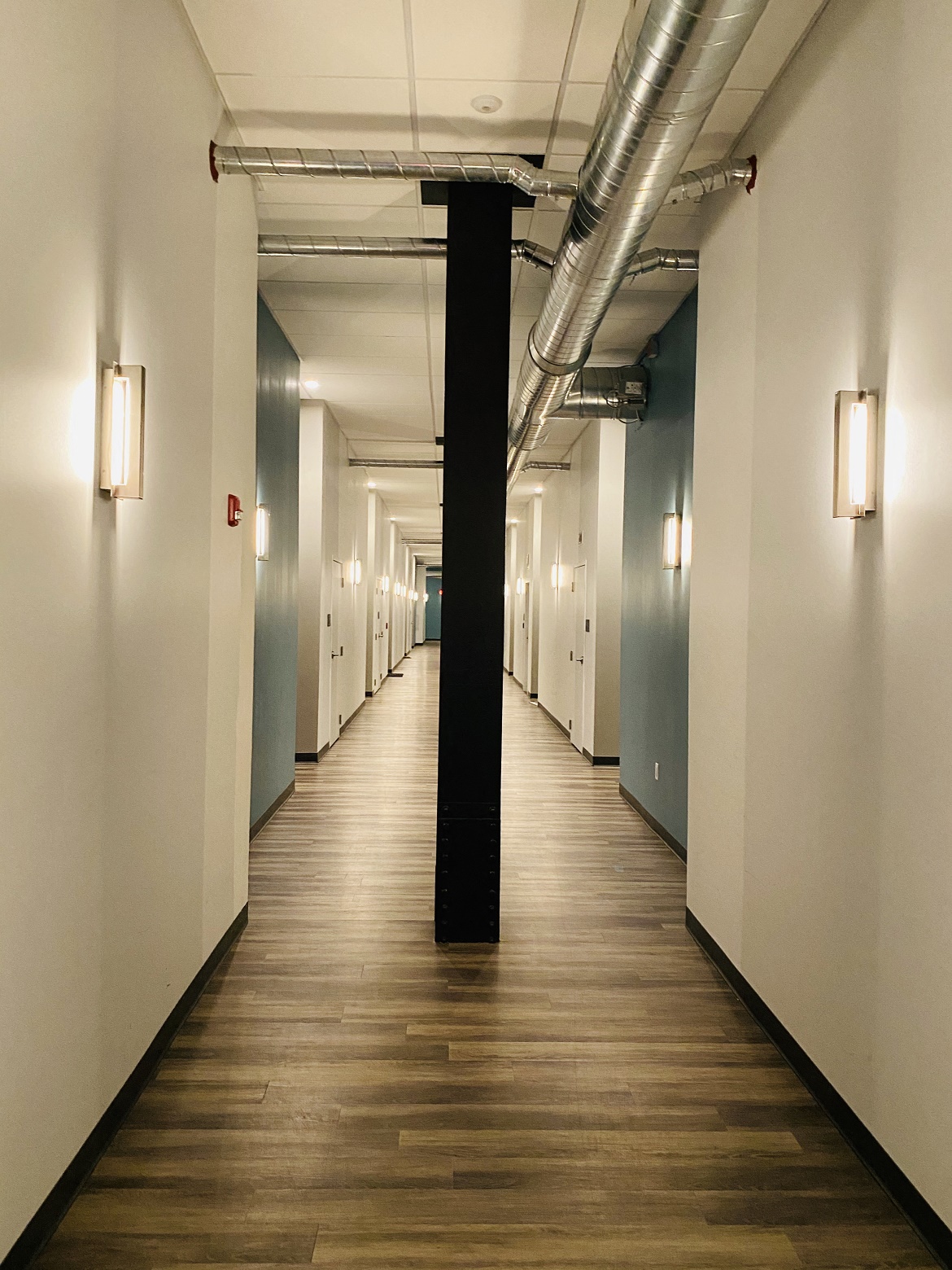 a long hallway with white walls and wooden floors and a black pillar in the middle