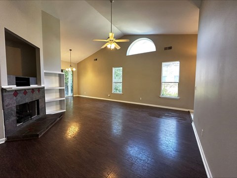 an empty living room with a fireplace and a ceiling fan