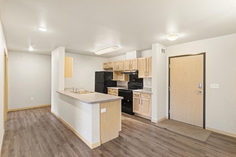 an empty living room with a kitchen and a door to a hallway