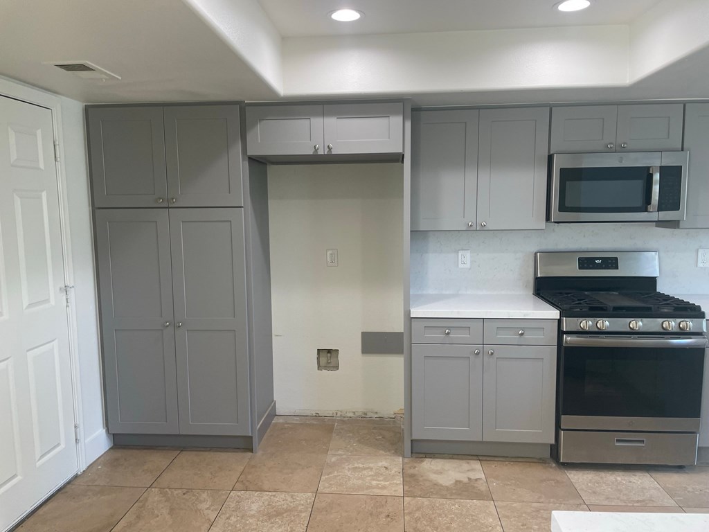 an empty kitchen with gray cabinets and stainless steel appliances